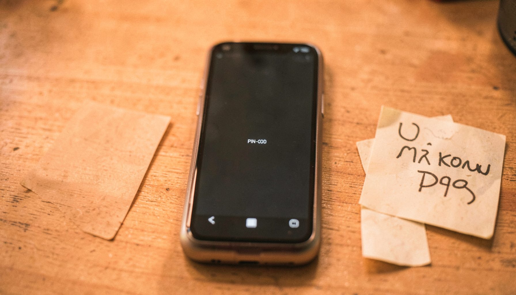 Jio F61F mudel, ekraanil PIN-koodi sisestusväli. Telefon on laual, kõrval on märkmik ja pliiats.