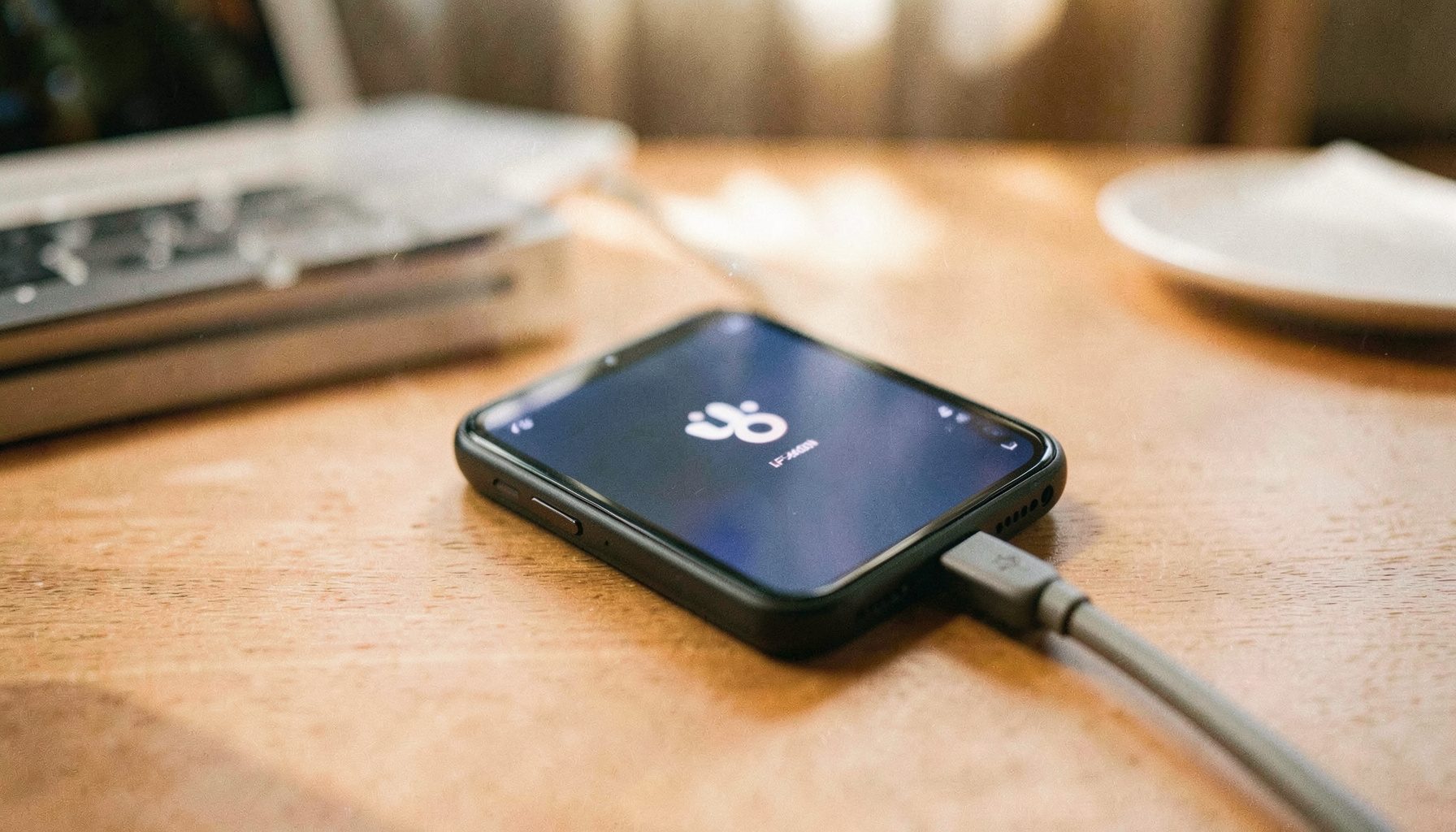 Jio Phone LF-2403N ekraanil logo, seade on ühendatud arvutiga USB kaabli kaudu. Taustal hämaras valguses töölaud.